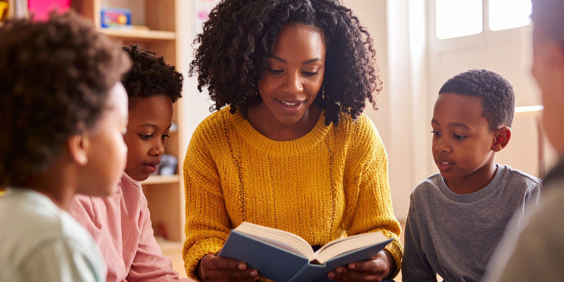 teacher reading to students who gather around her