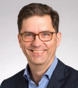 A headshot of Clark McKown, a male-presenting person, who smiles toward the camera.