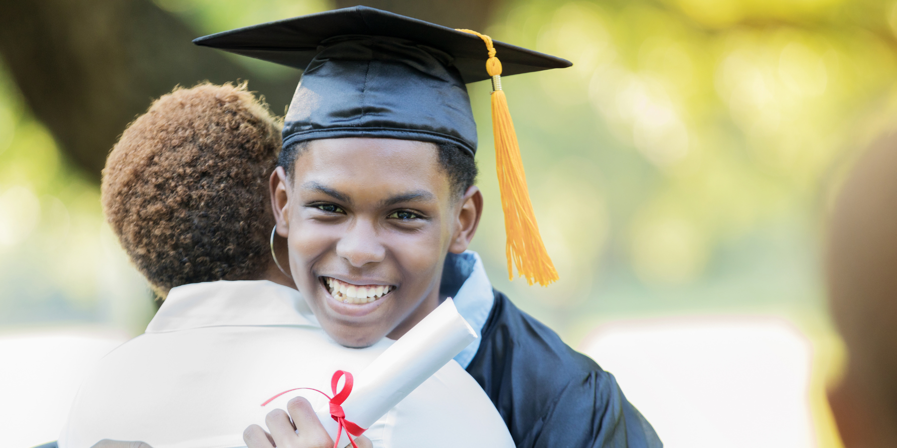 High school student with cap and diploma hugging his mother