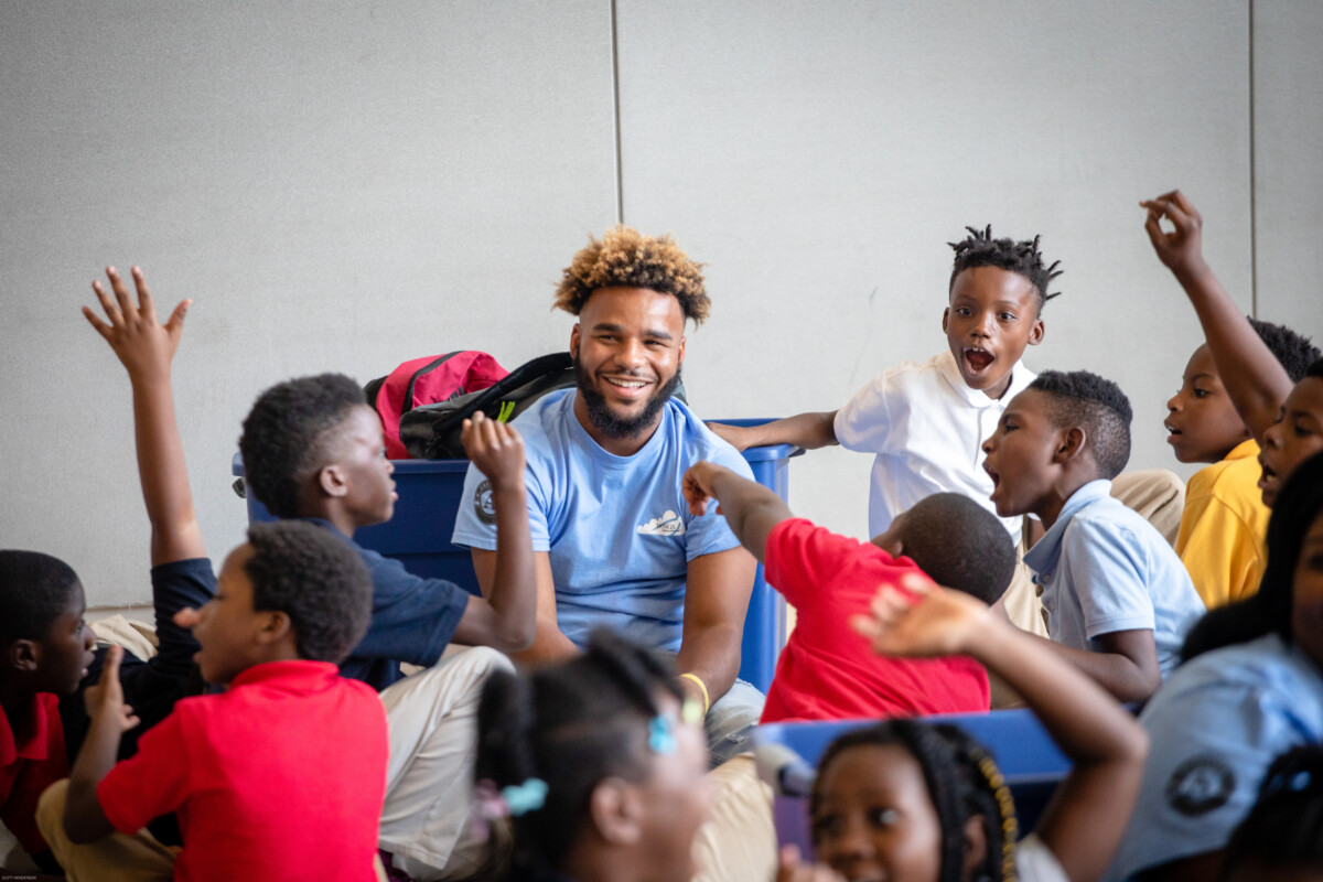 Male teacher center, surrounded by rambunctious students. All are smiling.