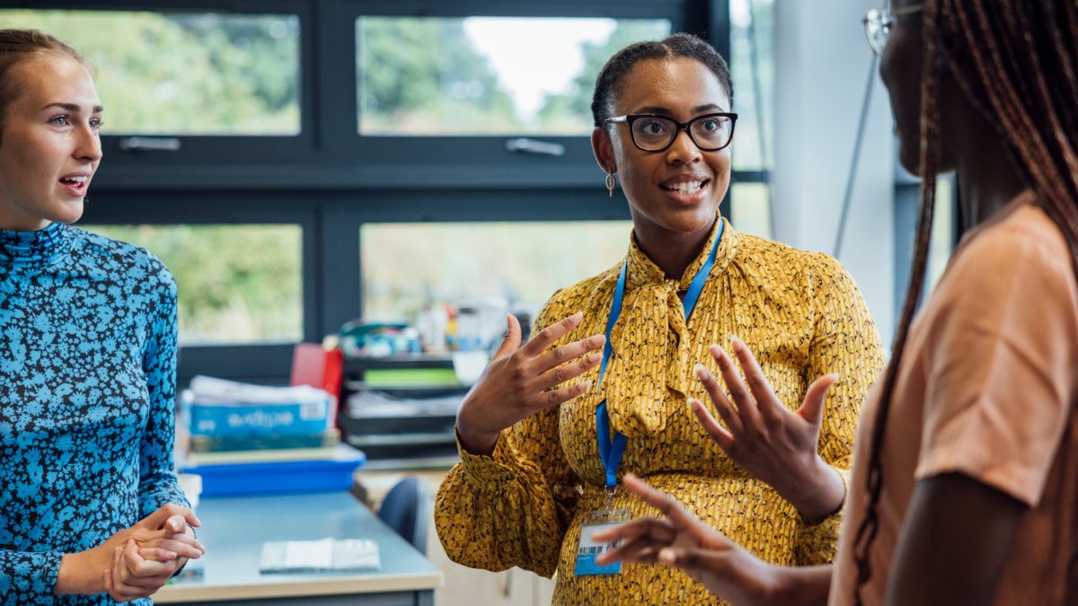 Three teachers talking excitedly at a table in a conference room