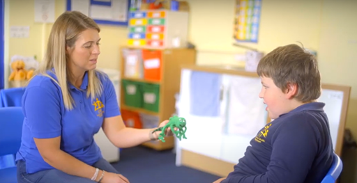 teacher holding out a zippy doll (cricket) to a young boy.