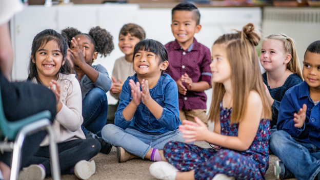 Happy kid in a classroom, sitting on rug and clapping