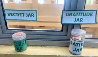 Picture of a window sill in a classroom with a jar labeled "Secret Jar" and a Jarl labeled "Gratitude Jar"